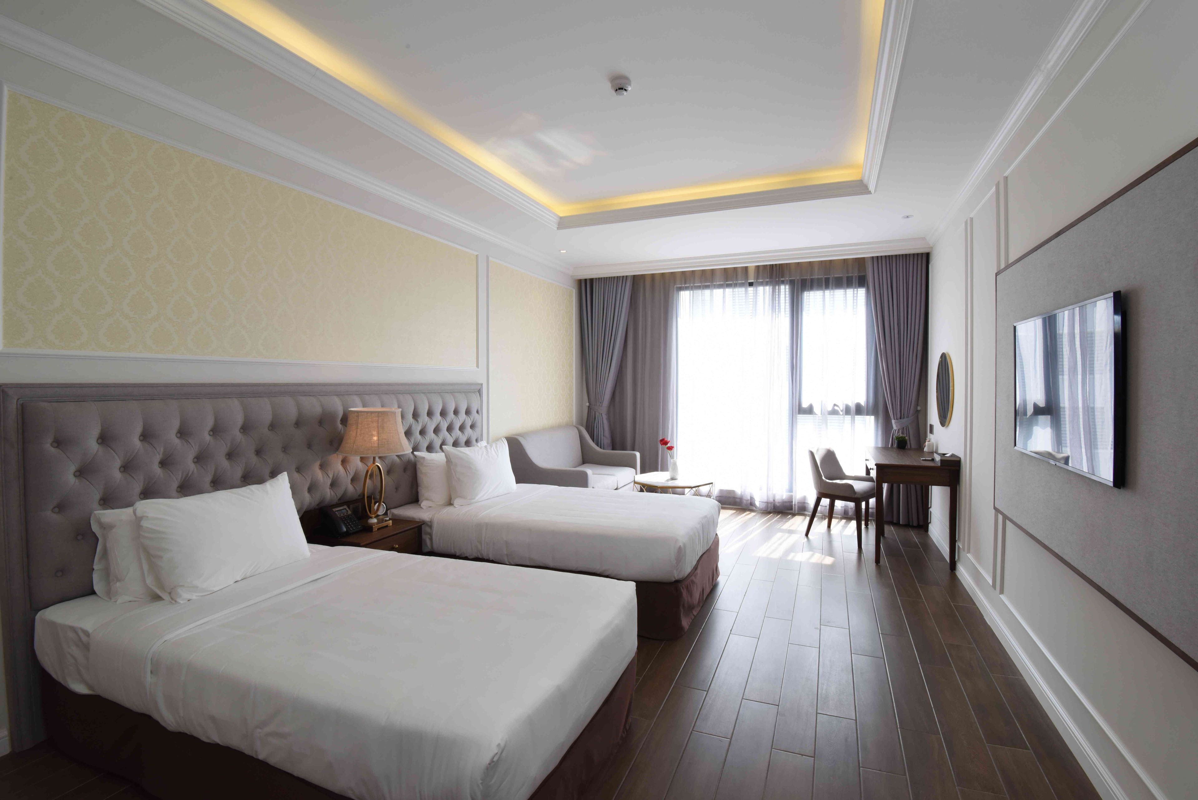 A hotel room with two beds, a desk, a chair, a TV, and a window with curtains.