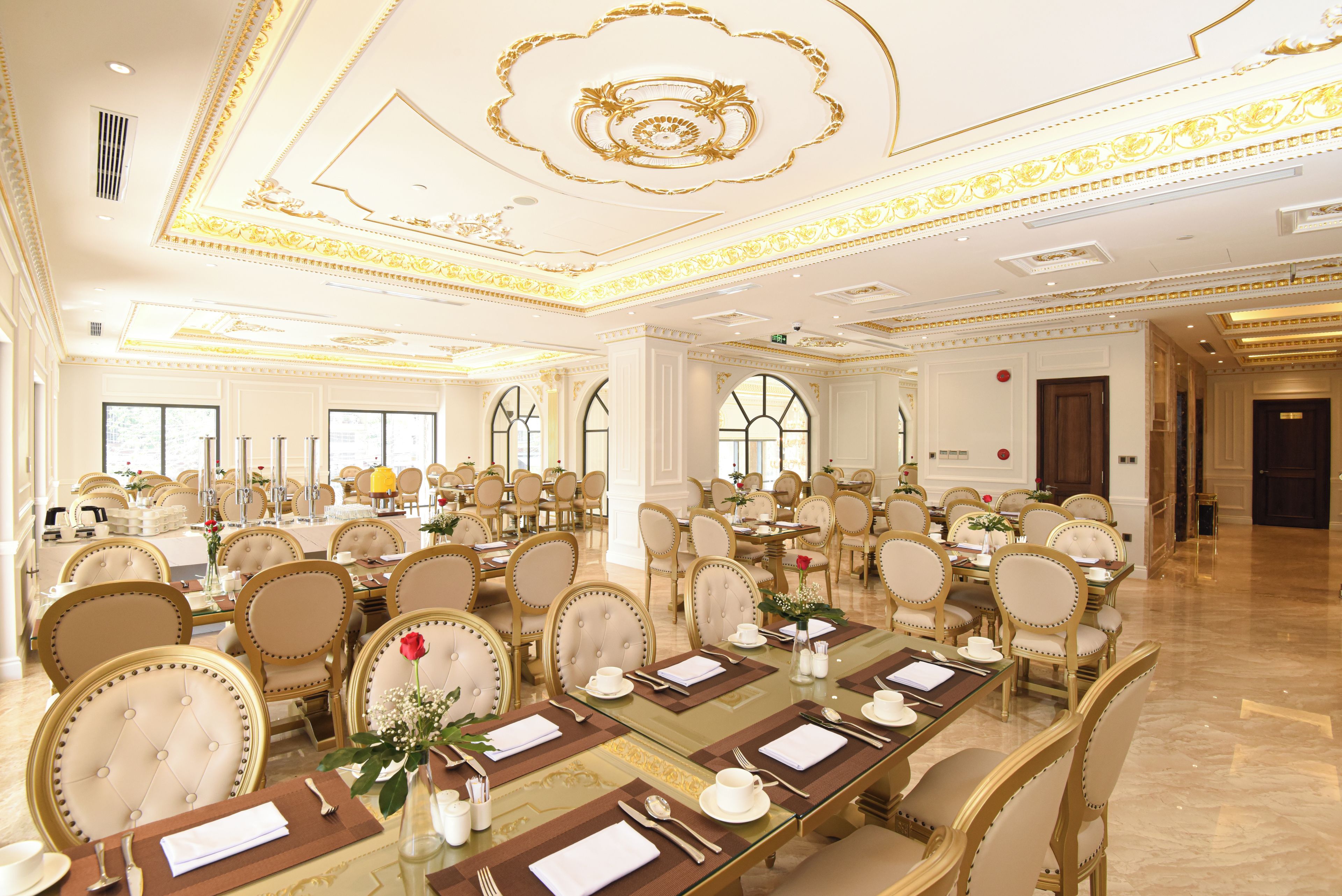 A large banquet hall with long tables set for dining, elegant chairs, and ornate ceiling decorations.