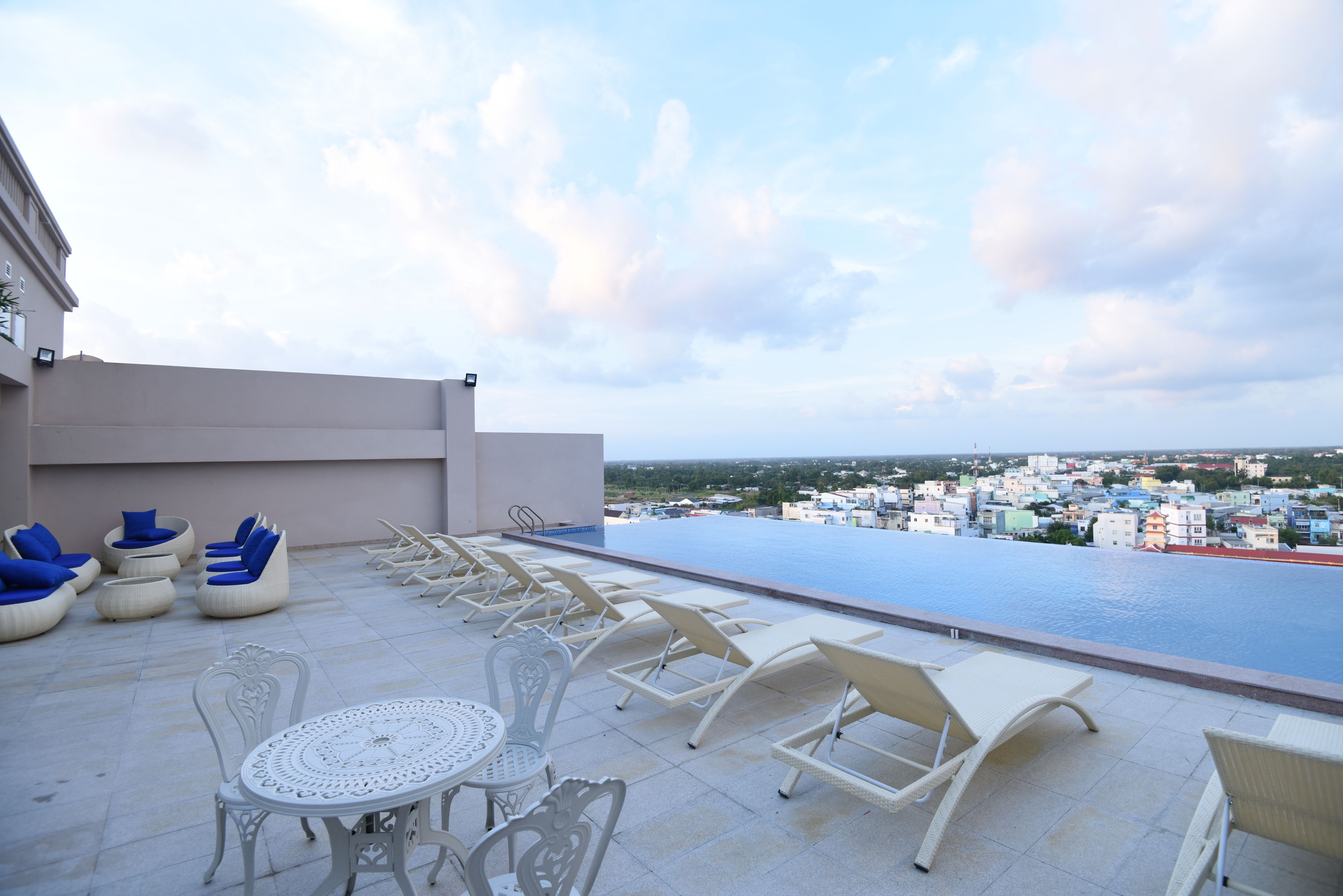 A rooftop pool area with lounge chairs and a table, overlooking a cityscape.