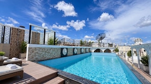 Une piscine avec une terrasse carrelée, des chaises longues et une pergola.