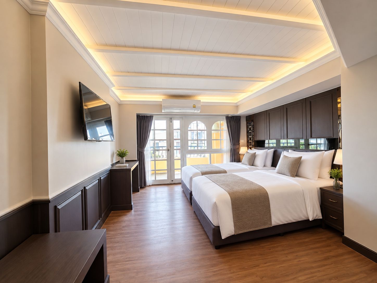 A hotel room with a large bed, a TV, a desk, and a balcony with curtains.