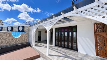 Un espace extérieur abrité, doté d’une pergola, d’une terrasse carrelée et d’une porte en bois.