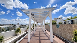 Une allée extérieure couverte, agrémentée d’une pergola, de plantes en pot et offrant une vue sur le paysage urbain.