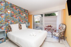 A hotel room with a bed, a chair, a small table, and a balcony with a view of buildings. - 3 Chambres 2 SDB Balcon Garage A3b139 (Cannes)