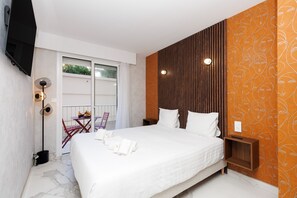 Ein Hotelzimmer mit einem Bett, einem kleinen Tisch mit Obst, einem Sessel, einem an der Wand befestigten Fernseher und einem Balkon mit Blick.
