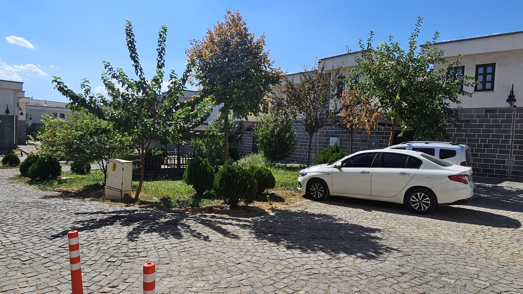 Un coche blanco estacionado en una calle adoquinada con árboles y un edificio al fondo.