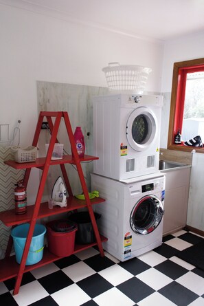 A laundry area with stacked appliances, a red shelf with cleaning supplies, and a checkered floor. - The Gap - Family Nature Retreat (Halls Gap)