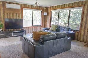 Een woonkamer met een leren bank, een flatscreen televisie en grote ramen.