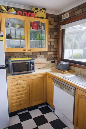 A kitchen with wooden cabinets, a microwave, a toaster, and a window. - The Gap - Family Nature Retreat (Halls Gap)
