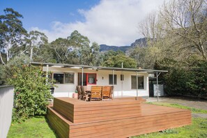 A single-story house with a patio, a dining area with wooden furniture, and a view of a mountainous landscape. - The Gap - Family Nature Retreat (Halls Gap)