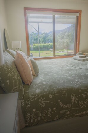 Een slaapkamer met een groot raam, een bed met bloemenbeddels en uitzicht op een tuin.