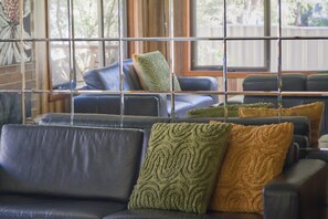Een zithoek met meerdere banken en stoelen, een raam met uitzicht op bomen, en een bakstenen muur.