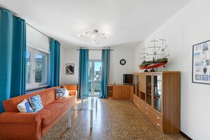 A living room with a sofa, a wooden cabinet with glass doors, a ship model, and a framed collage on the wall. - Apartment 'La Prua - Capitan Libeccio' with Lake View, Wi-Fi, and Air Conditioning (Garda)