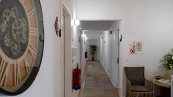 A hallway with a fire extinguisher, a clock, and a chair.