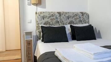 A bedroom with a bed, pillows, a bedside table, a lamp, and a door.