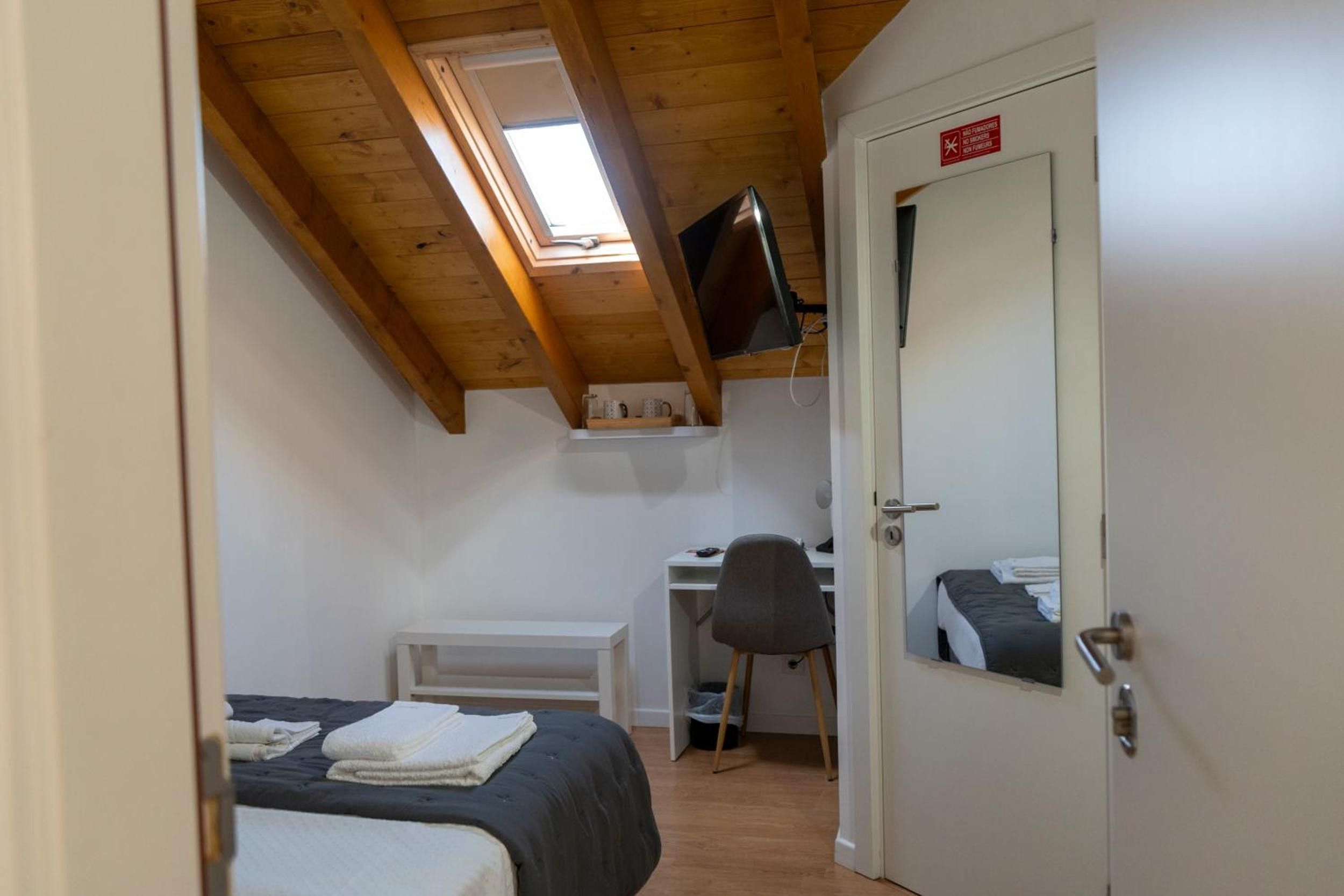 Una camera da letto con un letto, una scrivania, una sedia, una TV montata a soffitto e una porta con un cartello rosso.