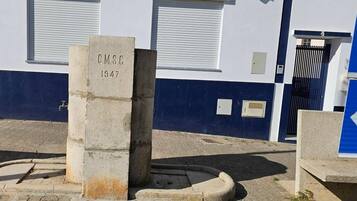 Un monument en béton portant l’inscription « C.M.S.C 1947 », situé devant un bâtiment à la façade bleue et blanche, avec une porte noire et une porte bleue.