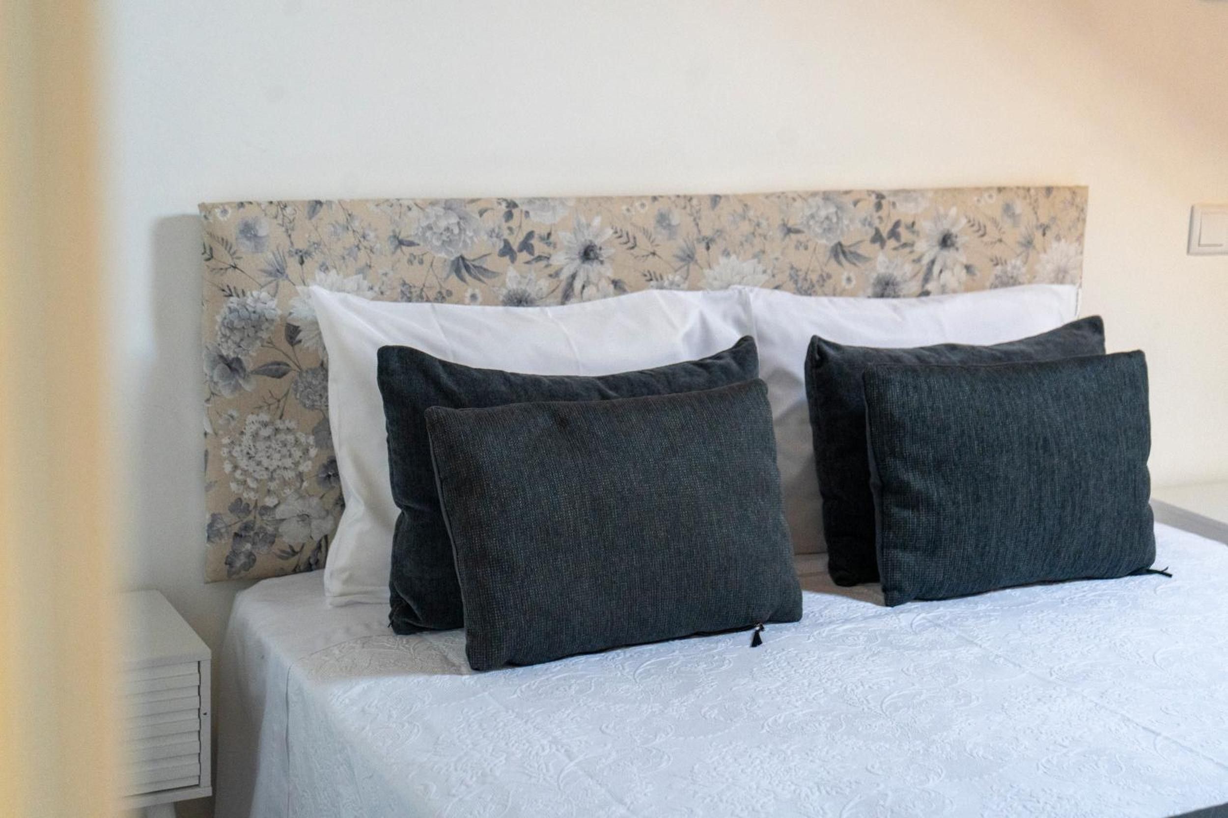 Un letto con testiera a motivi floreali, biancheria da letto bianca e due cuscini grigio scuro.
