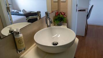A bathroom with a white sink, a mirror, a handheld soap dispenser, and a small potted plant.