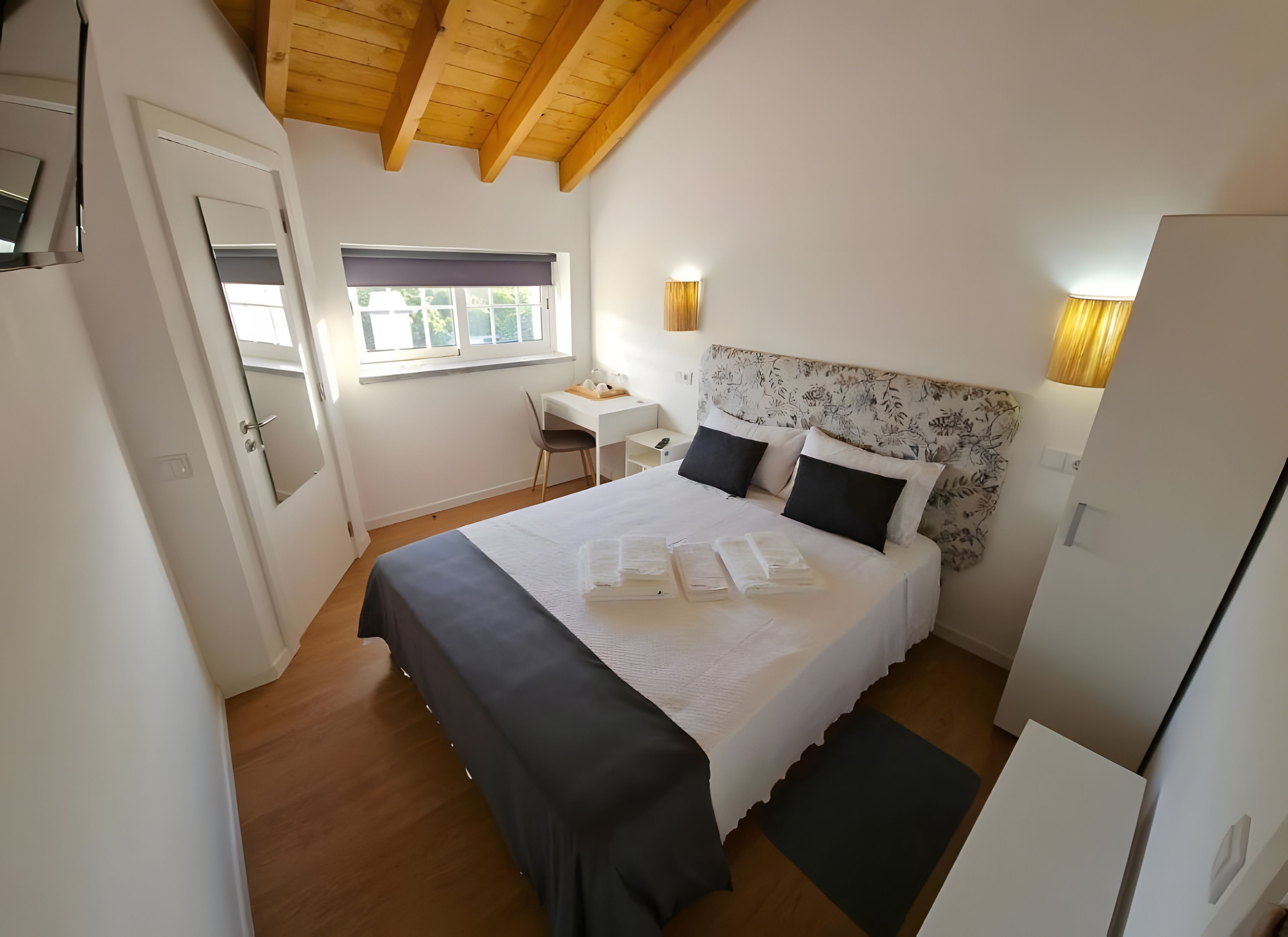A bedroom with a bed, bedside tables, a desk, and a window.