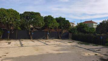 A parking area with trees and a fence, surrounded by buildings.