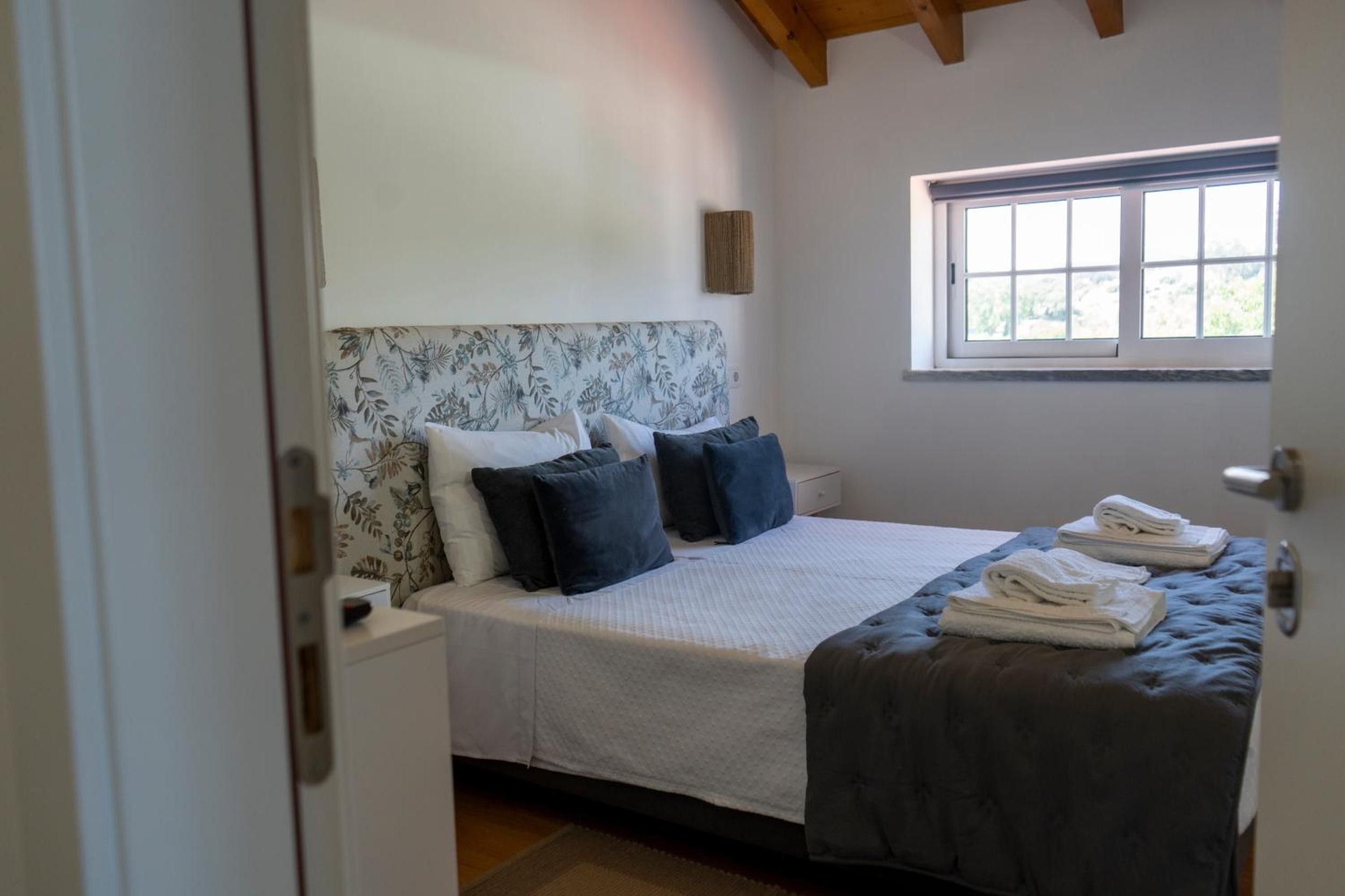 Een slaapkamer met een bed, kussens, een raam en een deur.