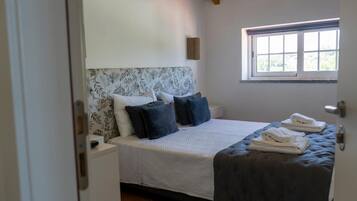 Een slaapkamer met een bed, kussens, een raam en een deur.