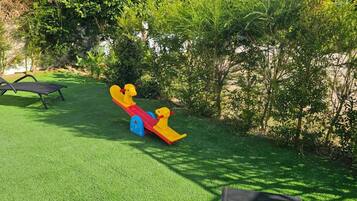 A playground with a seesaw and a black lounge chair on a grassy area.