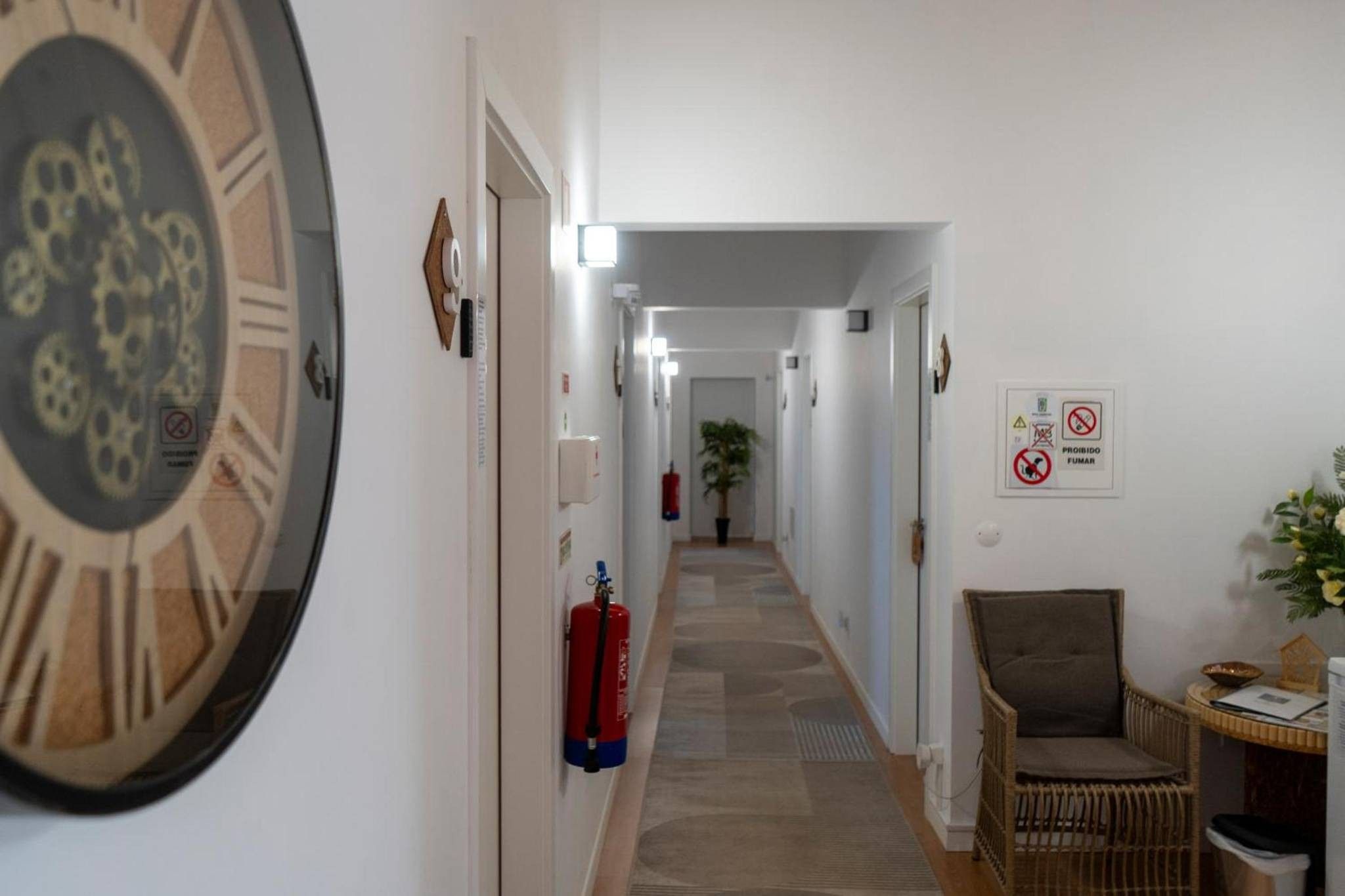 Un couloir avec un extincteur, une horloge et une chaise.
