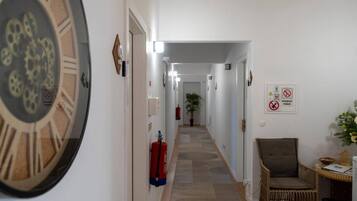 A hallway with a fire extinguisher, a clock, and a chair.