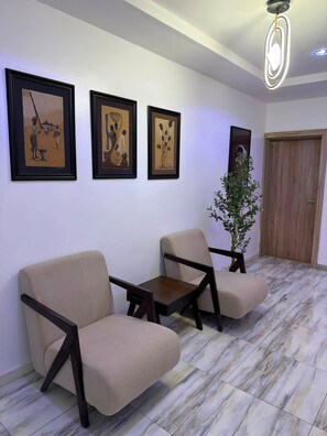 A waiting area with three chairs, a potted plant, and three framed artworks on the wall. - Vani's Apartment (Abuja)