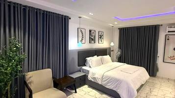 Et moderne hotelværelse med seng, sengebord, lampe, gardiner og en potteplante.