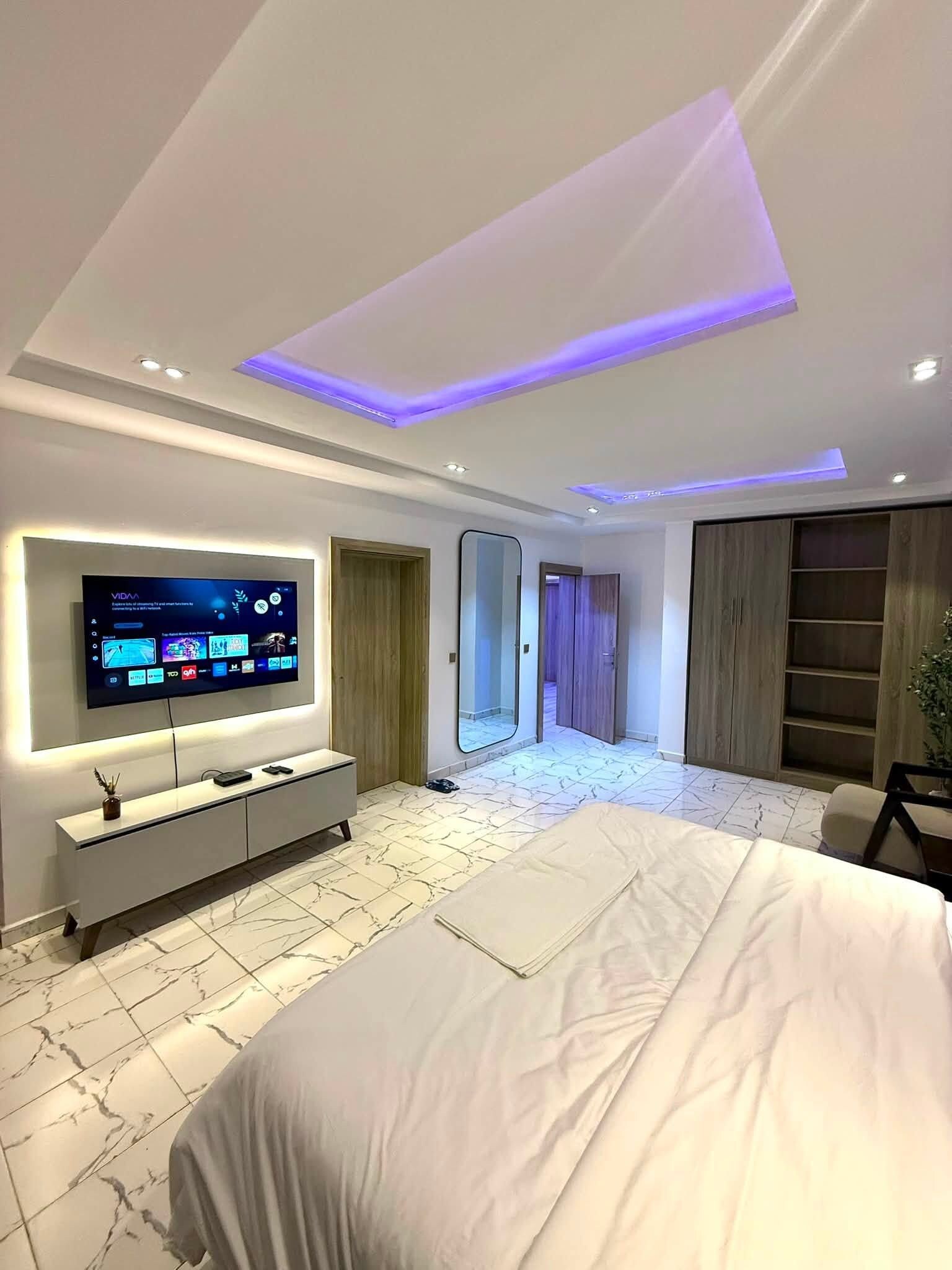 Un dormitorio moderno con una cama grande, un televisor montado en la pared y un vestidor.