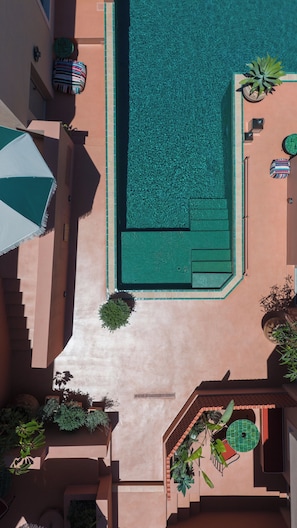 An aerial view of a swimming pool with a tiled deck, lounge chairs, and potted plants. - Terra Verde Oia Suites - Therra Grand Suite Sea View (Oia)
