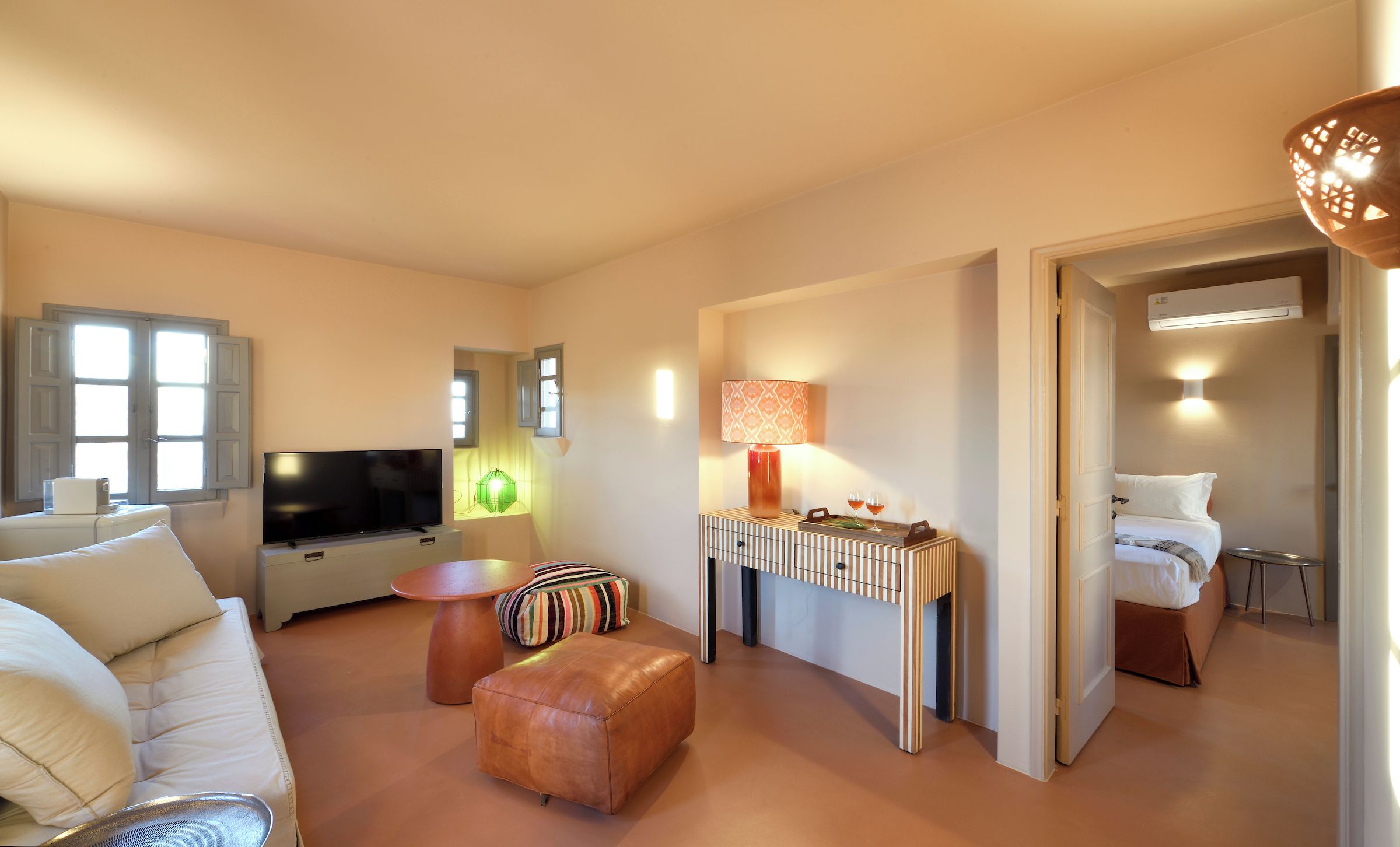 A modern hotel room with a sofa, a TV, a lamp, a small table, and a bed.