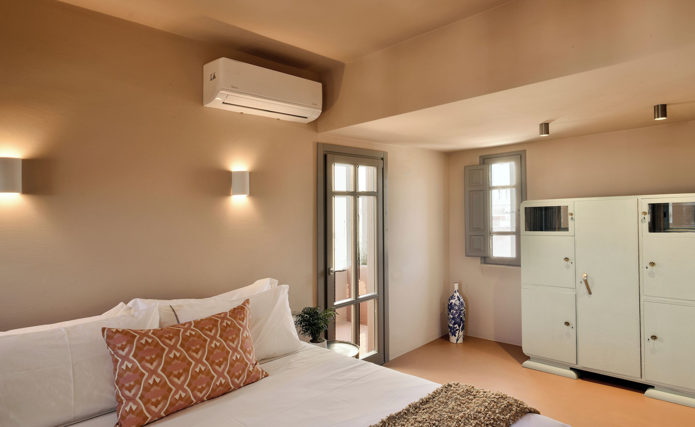 A bedroom with a bed, a wardrobe, an air conditioning unit, and a window.