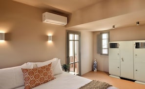 A bedroom with a bed, a wardrobe, an air conditioning unit, and a window. - Terra Verde Oia Suites - Therra Grand Suite Sea View (Oia)