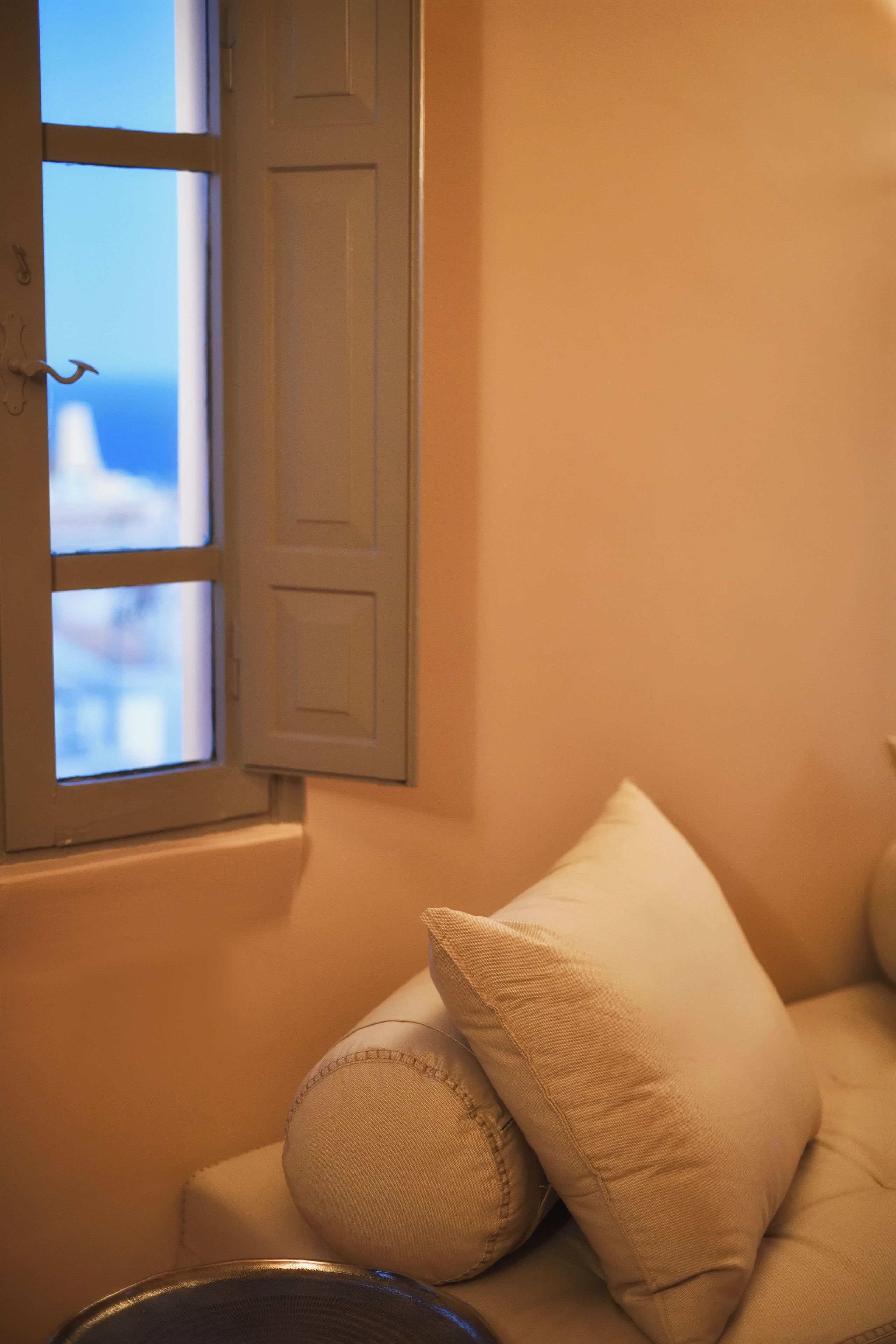 A room with a window, a white door, and a beige sofa with pillows.