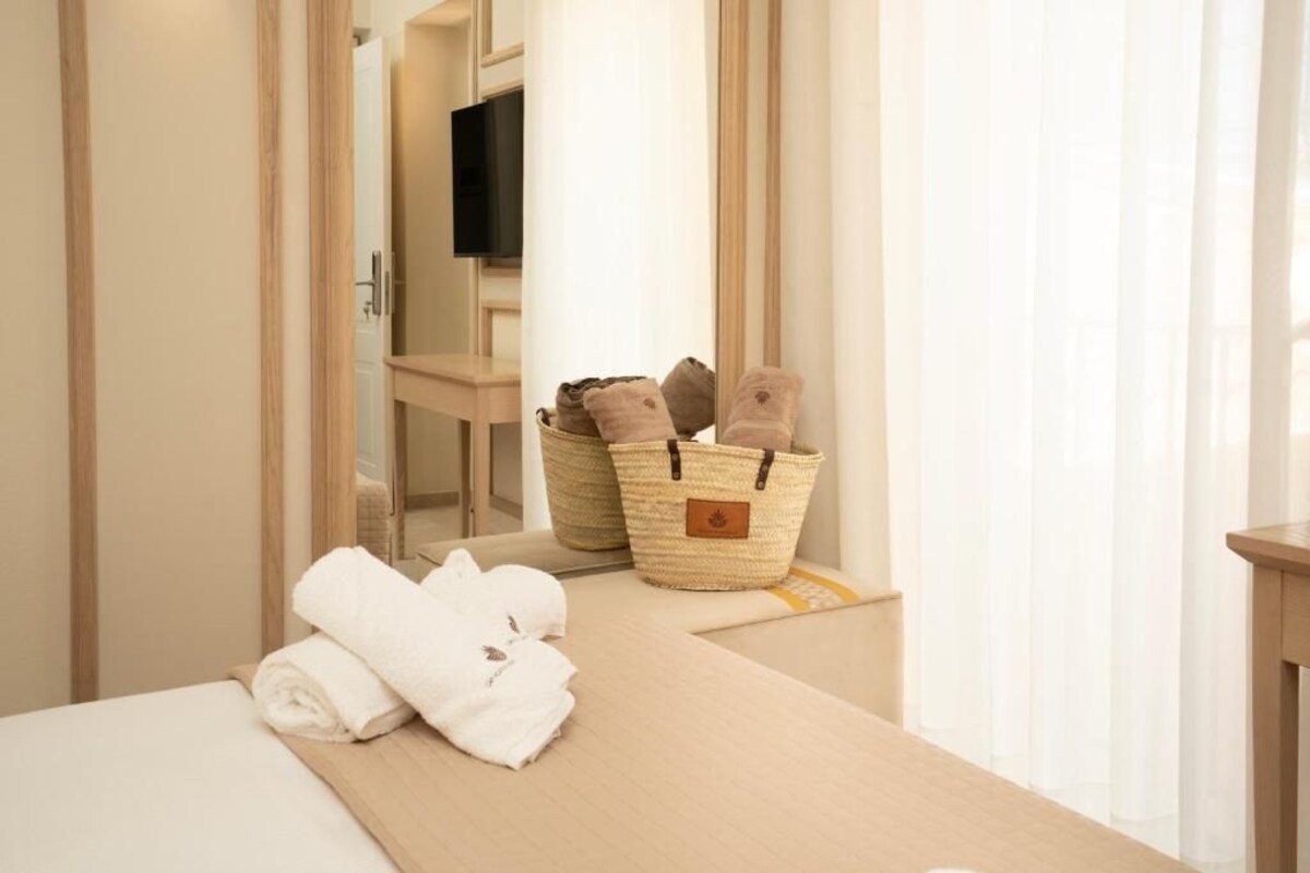 Habitación de hotel con cama, mesita de madera, televisor y dos cestas tejidas con toallas.