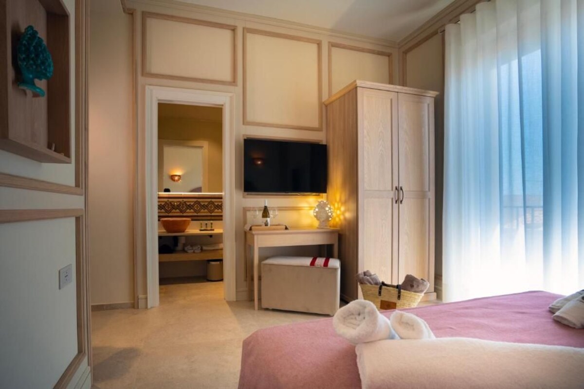 Habitación de hotel con cama, televisión, armario, escritorio con lámpara y ventana con cortinas.