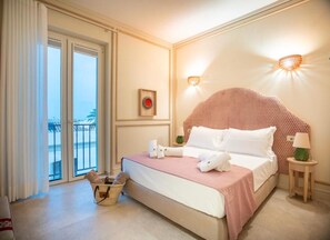 Habitación de hotel con cama, una mesita con lámpara, luz de pared, ventana con cortinas y vistas al exterior.