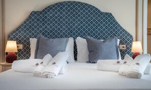 Habitación de hotel con cabecera estampada, dos almohadas, cama bien hecha con toallas y dos lámparas de noche.