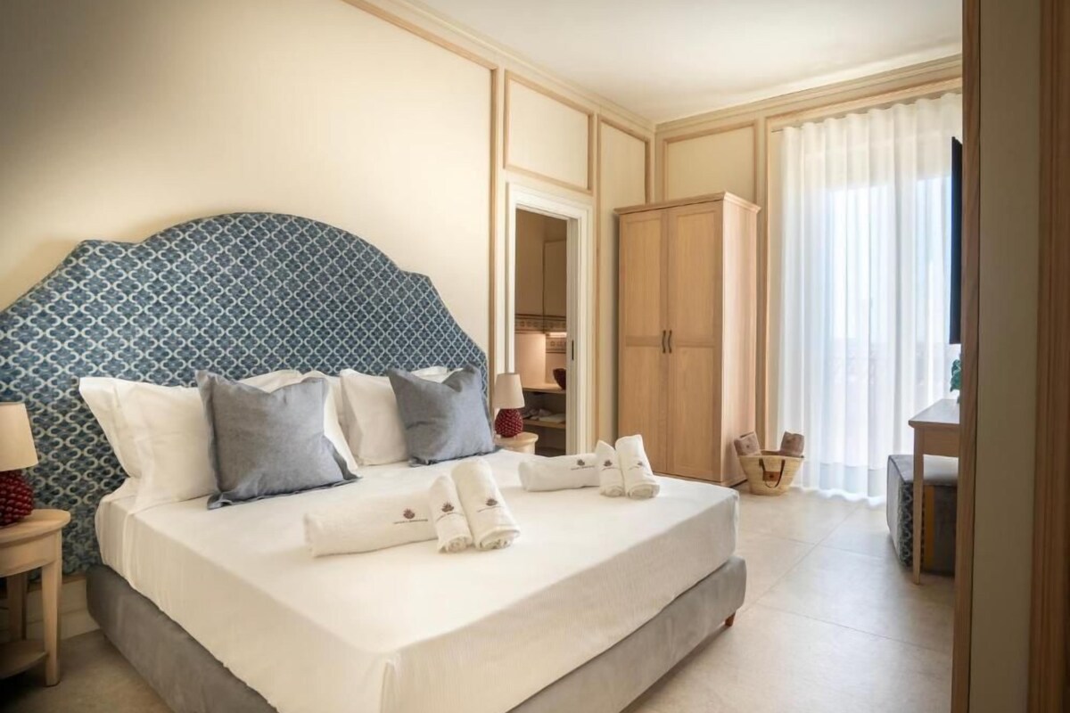 Habitación de hotel con una cama grande, un armario, un escritorio y un baño visible a través de una puerta abierta.