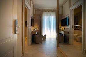 Habitación de hotel con un espejo grande, televisor, cama, mesita de noche y baño con inodoro y lavabo.