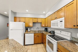 Una cocina compacta con muebles de madera, un refrigerador blanco, un microondas, un lavavajillas y una estufa.