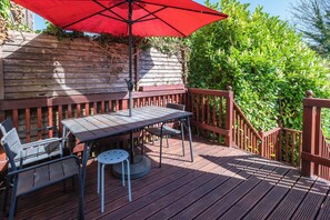 A wooden deck with a table and chairs, a red umbrella, and a wooden railing. - Modern 6-bed House in Bedford (Bedford)