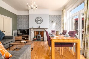 A living room with a fireplace, a dining table with chairs, a sofa, a television, and a chandelier. - Modern 6-bed House in Bedford (Bedford)