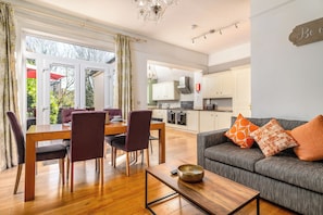 A modern living room with a sofa, coffee table, and dining area with chairs. - Modern 6-bed House in Bedford (Bedford)