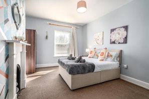 A bedroom with a bed, a window with curtains, a wall-mounted lamp, and a painting. - Modern 6-bed House in Bedford (Bedford)