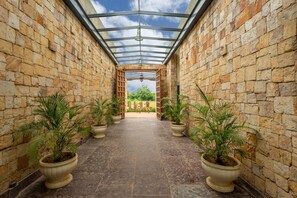 A covered walkway with stone walls, potted plants, and a bicycle in the distance.